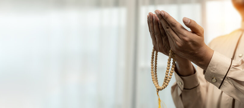 Hand holding muslim beads rosary or tasbih isolated on white background.. Religious arab muslim man holding holy quran. Muslim man standing with hands raised and praying against indoor daytime scene. 