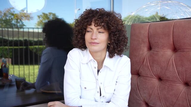 Thoughtful Woman Sitting in a Modern Caf with Curly Hair