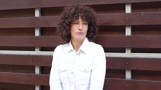 A contemplative woman with curly hair poses thoughtfully in an urban outdoor setting