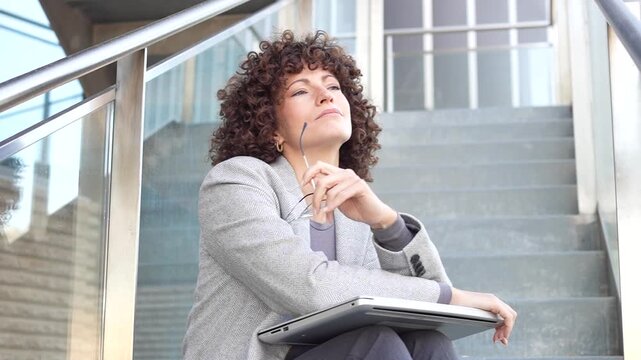 A businesswoman sits on stairs with her laptop, contemplating ideas and strategies for success