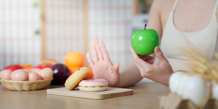 Cropped hand holding green apple and rejecting donuts for healthy eating choice