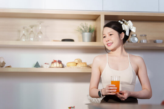 Asian woman holding glass of fresh orange juice in kitchen for healthy lifestyle