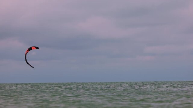 Action shot of a lone kitesurfer on Wingfoil with kite gliding across rough ocean waters on an overcast day. Extreme water sports and active lifestyle concept. Flying over water in slow motion..