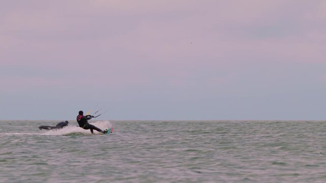 Action shot of a lone kitesurfer with kite gliding across rough ocean waters on an overcast day. Extreme water sports and active lifestyle concept. Flying over water in slow motion..