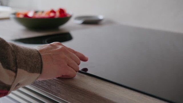 Close-up of a person turning on an induction cooktop and placing a frying pan on the burner in a modern kitchen.