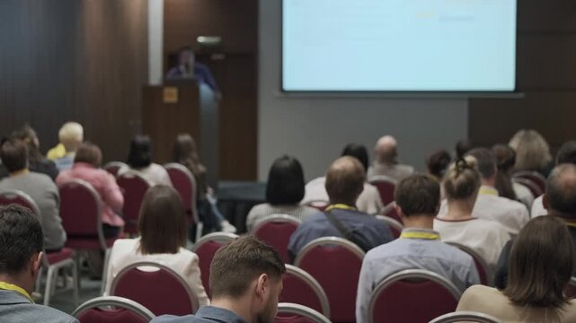 Conference attendees seated listening to presenter at front, slideshow visible, professional seminar atmosphere, networking and learning in modern meeting room.