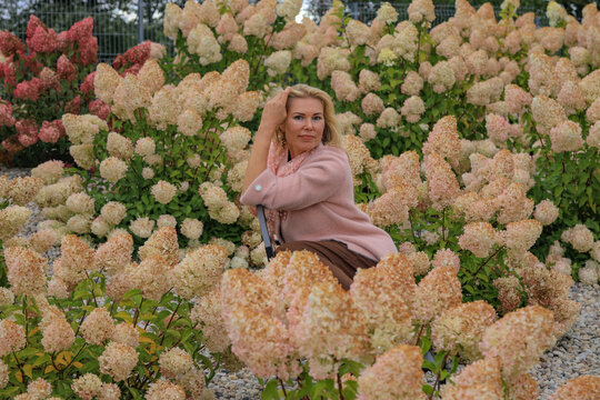 Elegant mature woman posing among pastel hydrangeas in autumn garden