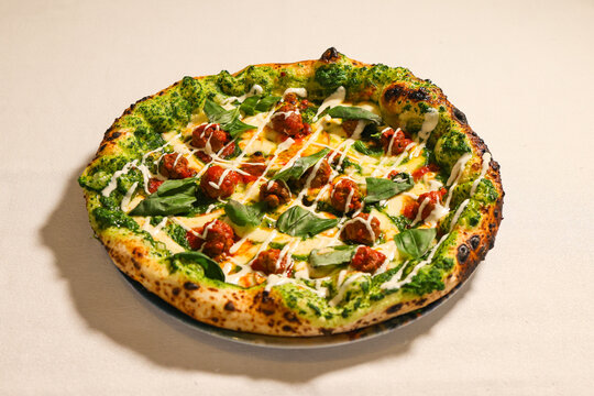 Gourmet Neapolitan-style pizza topped with meatballs in tomato sauce, melted cheese, green herb sauce, fresh basil and creamy white drizzle.