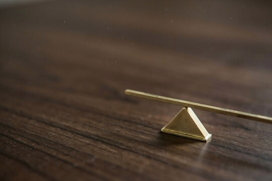 Miniature brass balance beam on a pyramid fulcrum across dark polished walnut