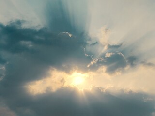 Sunbeams burst through dense cloud layers in a cool teal sky, creating a striking contrast of warm light and shadowed weather. © choyi