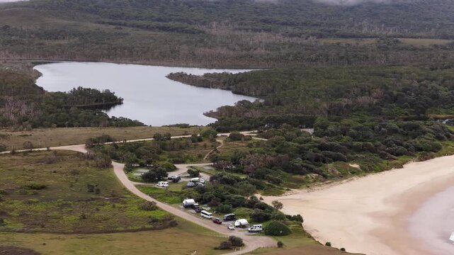 Aerial video flying over the rugged coastline at Lake Arragan, featuring sandy shoreline, rocky formations and waves rolling in from the Pacific Ocean
