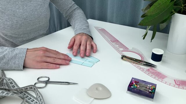 The woman lays out a small skirt pattern on a white table; the lady is learning to work with the clothing mockup and sewing supplies. The concept of acquiring a new hobby and practical skills