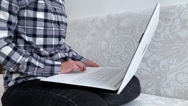 The woman is completing work tasks on a laptop in a comfortable home environment. The topic is the modern employment format, freelancing, independent work, and mobile office. Side view