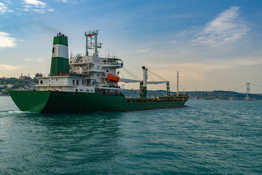 Green cargo ship sailing on the Bosphorus strait in Istanbul with city skyline and bridge background