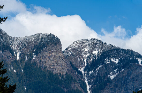 Snow-dusted rugged mountain peaks and evergreen forest under a blue cloudy sky