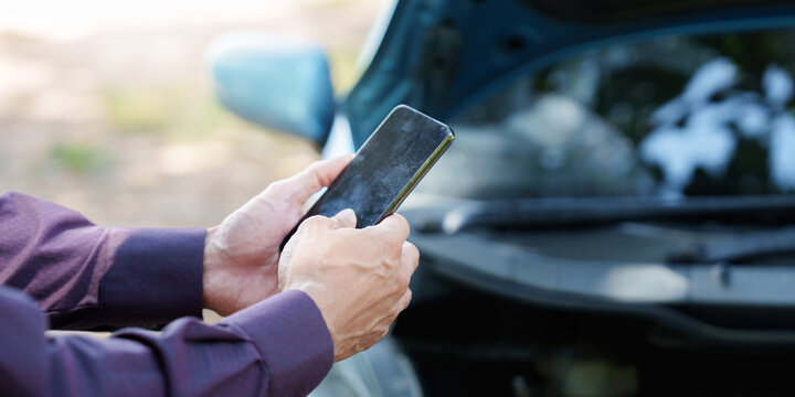 Cropped hands holding smartphone near broken car for insurance claim