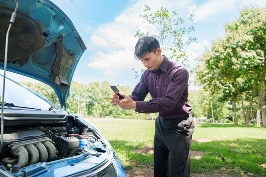Asian man taking photo of broken car engine with smartphone for insurance