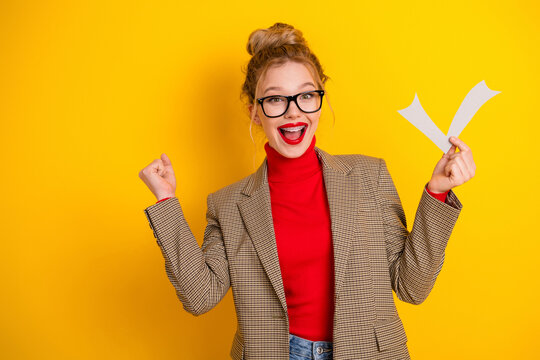 Cheerful young businesswoman holding a paper showing success gesture against vibrant yellow background