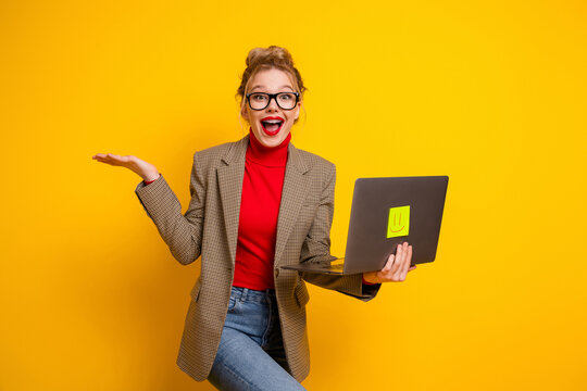 Charming young woman in blazer holding laptop on yellow background presenting idea with happy and surprised gesture
