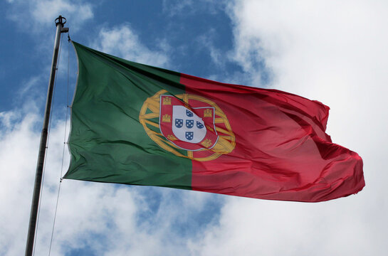 flag of portugal blowing in the wind on a blue sky and white cloud background