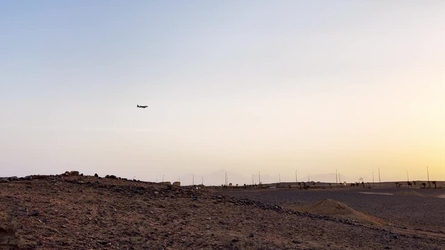 Airplane flying across the golden sunset sky over a desert landscape