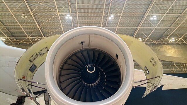 Close-up aircraft turbofan engine with fan blades and open cowling inside a hangar during maintenance inspection, showcasing modern commercial aviation engineering and engine technology