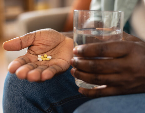Hand holding pills with glass of water at home