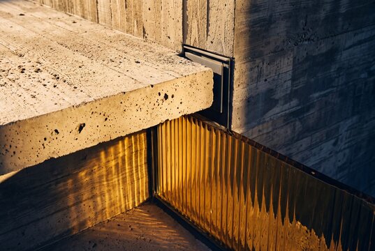 Architectural detail of concrete steps and textured amber glass railing illuminated by warm sunlight