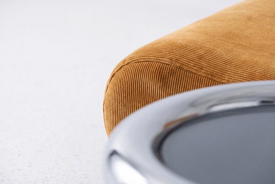 Close-up detail of mustard yellow corduroy fabric sofa and curved chrome coffee table in modern minimalist interior
