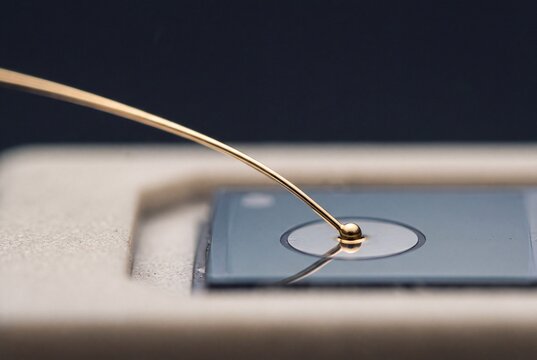Macro shot of a microchip wire bonding process showing a precision gold wire attached to a semiconductor pad