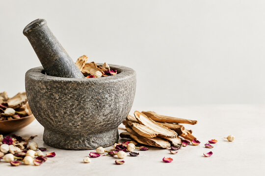 Stone mortar and pestle with dried mandrake roots and petals, herbal apothecary still life
