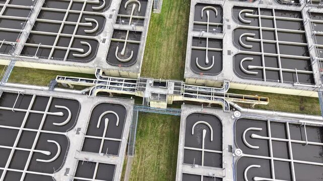 Aerial view of wastewater treatment facility showing multiple treatment tanks with flowing water and interconnected piping systems in a city environment. Ecology and recycling concept