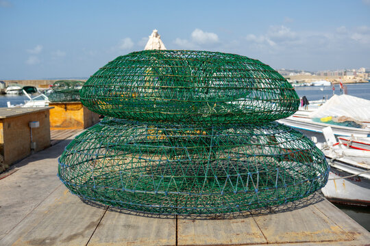 Green wire fish traps are stacked on a wooden pier overlooking the fishing harbor, South Governorate, Tyre, Lebanon