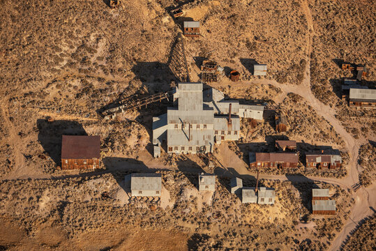 Aerial view of Bodie, a historic gold-mining ghost town with weathered wooden buildings, rusted mining equipment, and dirt paths in Mono County, California, United States.