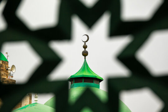 A green mosque dome topped with a crescent finial appears through a pierced star-patterned screen, North Governorate, Tripoli, Lebanon