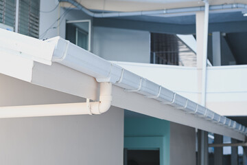 White plastic rain gutter system installed on building roof. © Aphisith