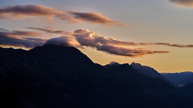 Aerial view of Valchiavenna mountain range at sunset with dramatic clouds and silhouettes over the peaks in Lombardy, Italy.
