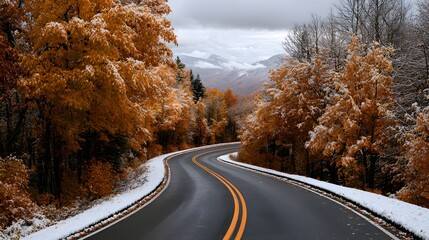 Obraz premium Winding asphalt road through a scenic mountain forest with autumn foliage and a light dusting of fresh snow