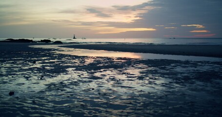 Fototapeta premium A serene coastal landscape at low tide reflects the beautiful twilight sky in tidal pools, with distant fishing boats on the calm ocean creating a peaceful travel scene.