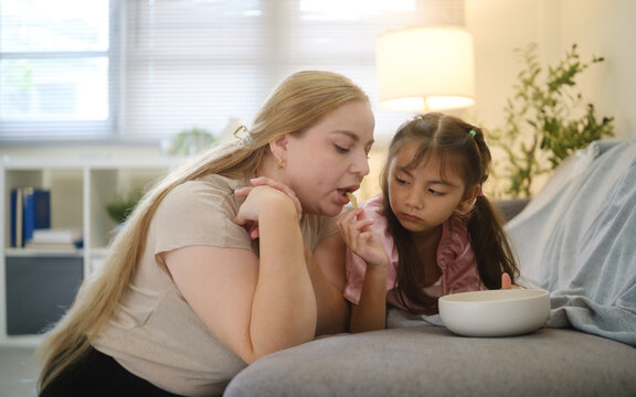Woman and young girl sharing snacks while relaxing together on a sofa.