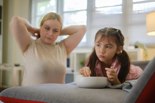 Woman and young girl sharing snacks while relaxing together on a sofa.