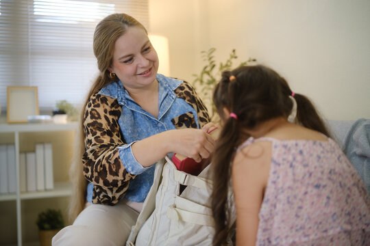 Woman helping a young girl pack and prepare a backpack at home.