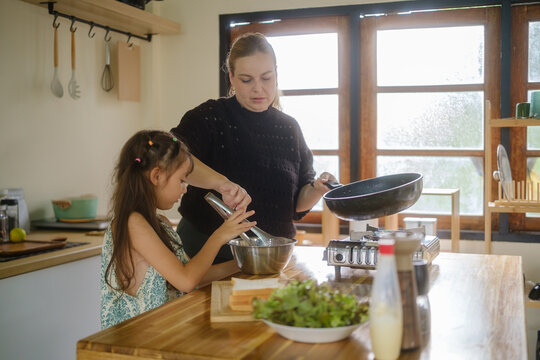Woman and young girl preparing a meal together in a home kitchen.