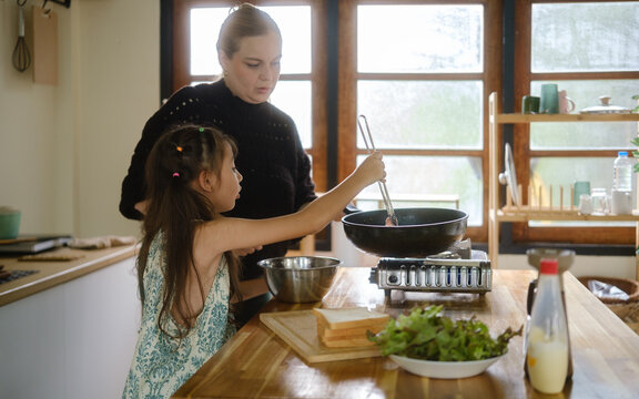 Woman and young girl preparing a meal together in a home kitchen.
