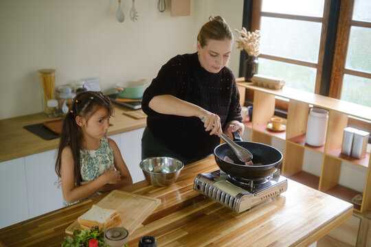 Woman and young girl preparing a meal together in a home kitchen.