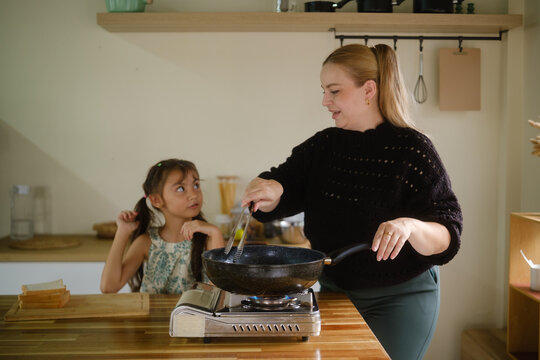 Woman teaching a young girl to cook a healthy meal in the kitchen.