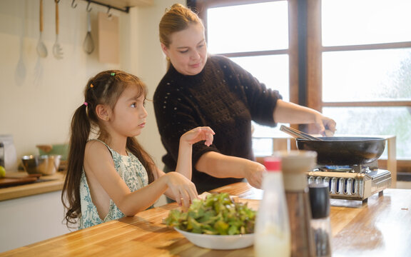 Woman teaching a young girl to cook a healthy meal in the kitchen.