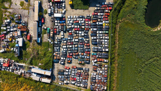 Aerial view of a car scrapyard with rows of wrecked vehicles, scrap metal, and industrial debris in Milan, Lombardy, Italy.