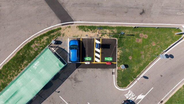 Aerial view of an electric car charging station with a blue vehicle parked in a designated space marked with green symbols in Milan, Lombardy, Italy.