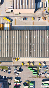 Aerial view of the DHL Express facility featuring a large warehouse with a corrugated roof, loading docks with yellow trucks, and a parking area in San Giuliano Milanese, Lombardia, Italy.